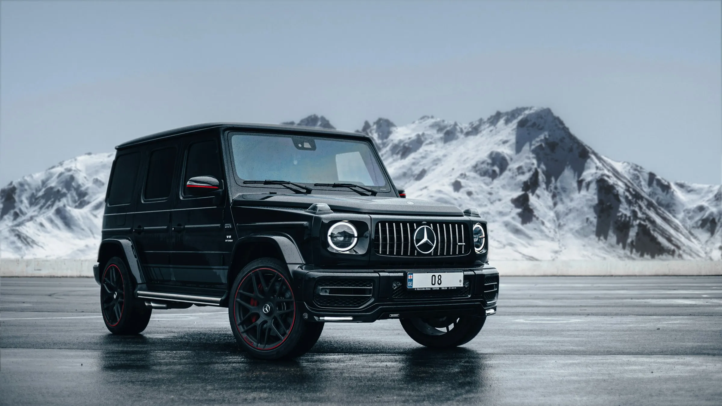 Todoterreno Mercedes-Benz negro sobre asfalto mojado frente a montañas nevadas